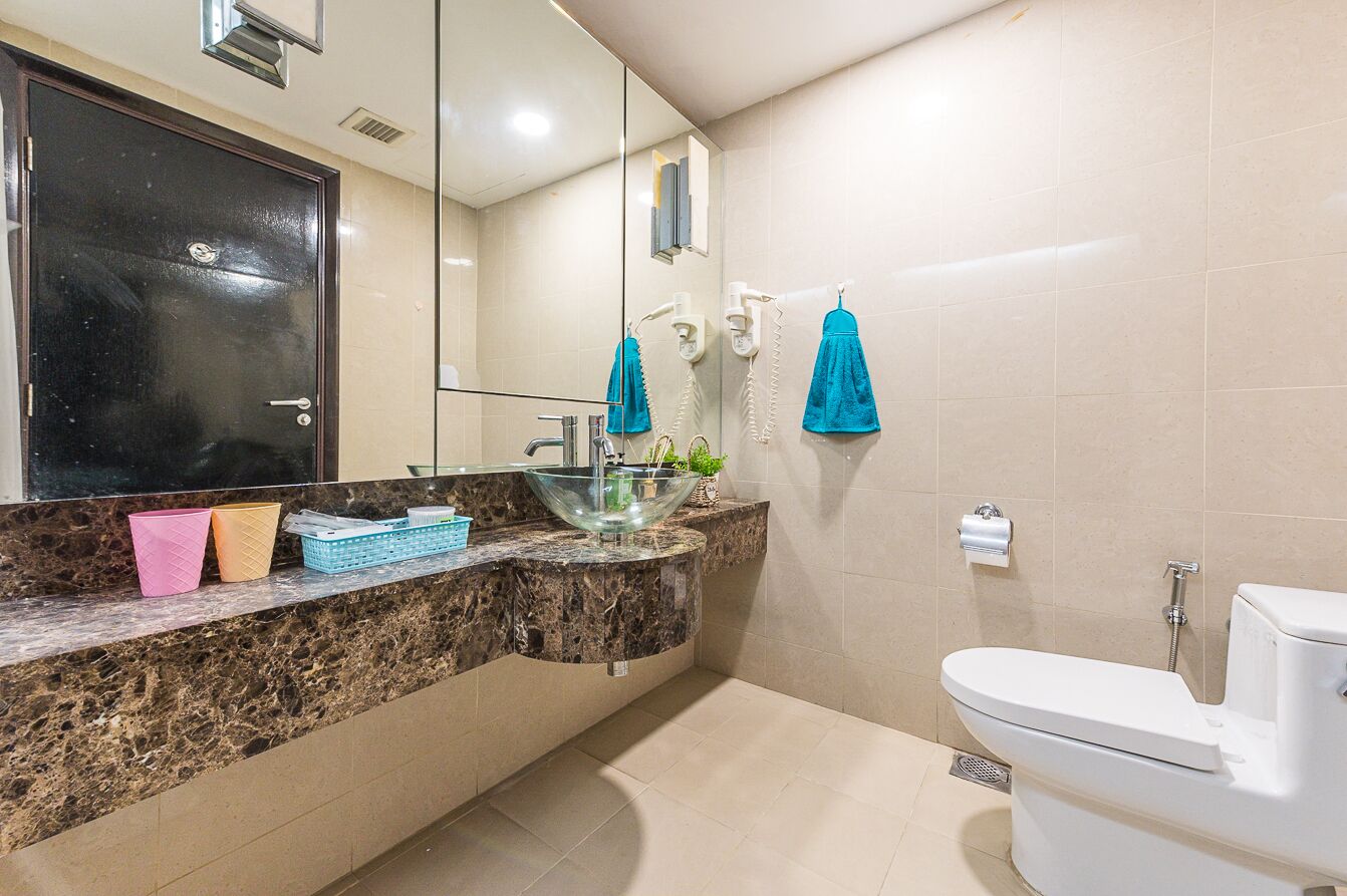 A bathroom with a marble countertop, a glass bowl sink, a toilet, and a mirror.