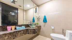A bathroom with a marble countertop, a glass bowl sink, a toilet, and a mirror.