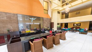 A hotel reception area with a modern design, featuring a reception desk, seating area, and a balcony with a railing.