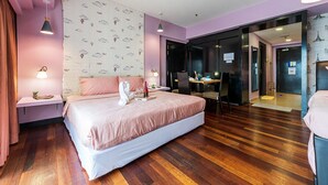 A modern hotel room with a large bed, wooden flooring, and a desk area with a computer.