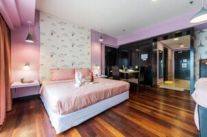 A modern hotel room with a large bed, wooden flooring, and a desk area with a computer.