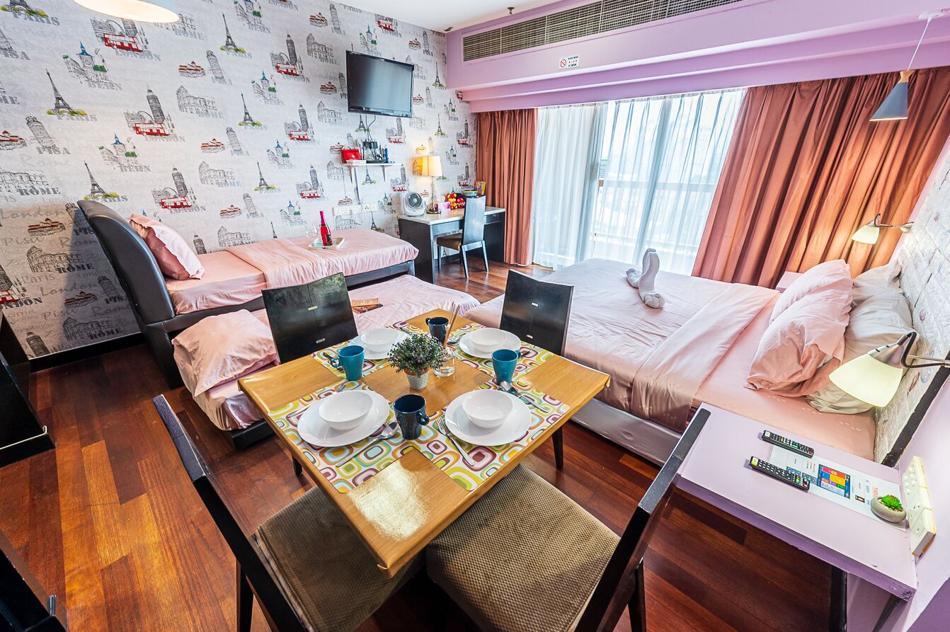 A hotel room with a bed, a desk, a chair, a table with a plant, and a TV on the wall.