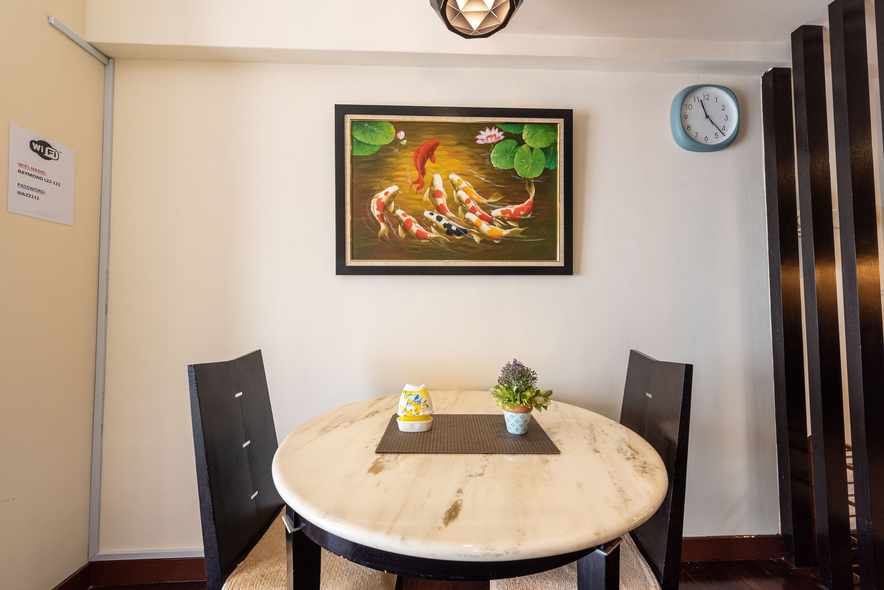 Ein Essbereich mit einem runden Tisch, zwei Stühlen, einer Uhr und einem gerahmten Bild von Koi-Karpfen.