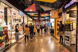 Un pasillo de centro comercial con diversas tiendas, incluyendo una de ropa con maniquíes y un cartel que dice 'MPSY'.