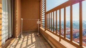 A balcony with a metal railing, a mop leaning against the wall, and a view of a cityscape.