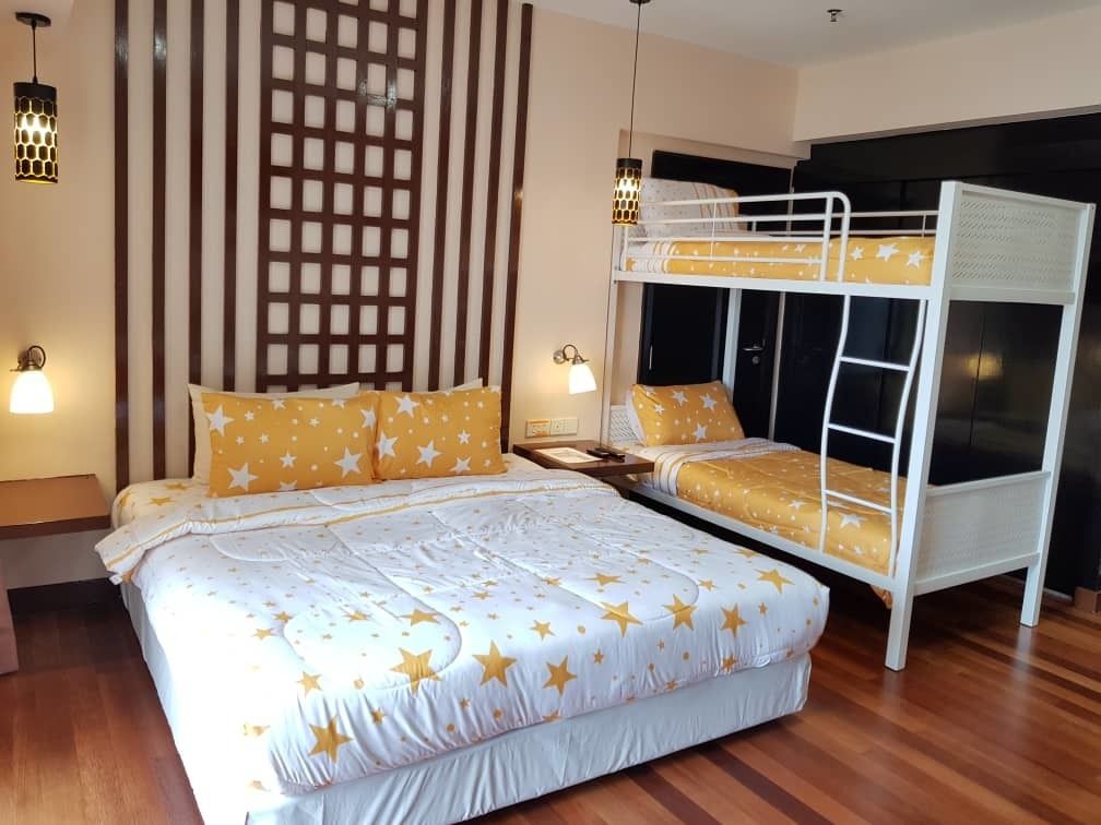 Un dormitorio con literas, una cama grande con ropa de cama estampada de estrellas, suelo de madera y dos lámparas fijadas a la pared.