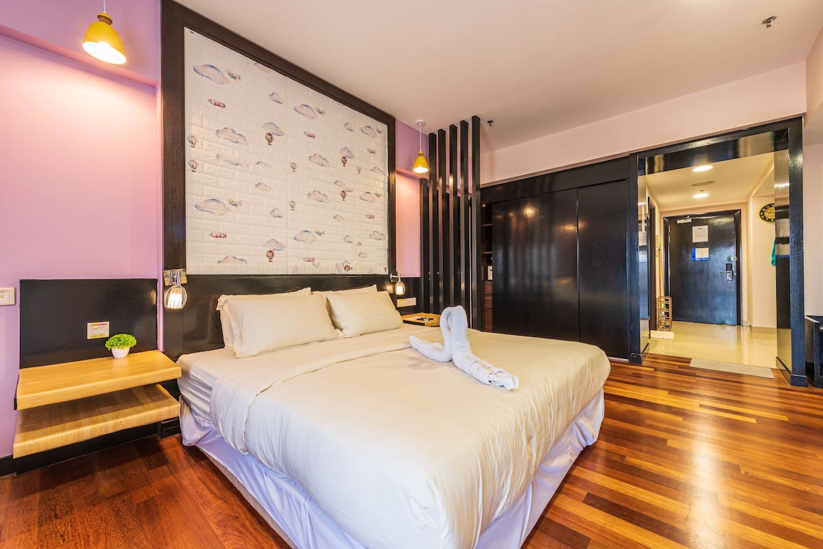 A modern hotel room with a large bed, wooden flooring, a wall with a cloud pattern, and a sliding door leading to another room.