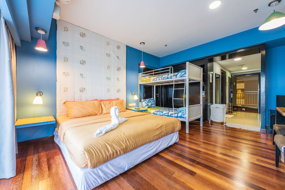 A bedroom with a bunk bed, a large bed, wooden flooring, a wall with decorative plates, and a sliding door leading to another room.