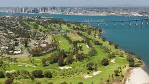 An aerial view of a coastal golf course with a bridge in the background.