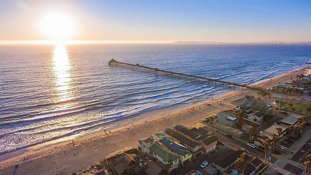 A coastal area with a pier extending into the ocean, beachfront properties, and a clear sky.