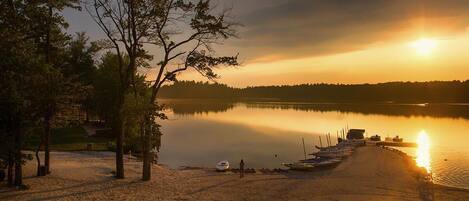 A lakeside scene with a sandy beach, trees, and boats docked along the shore.