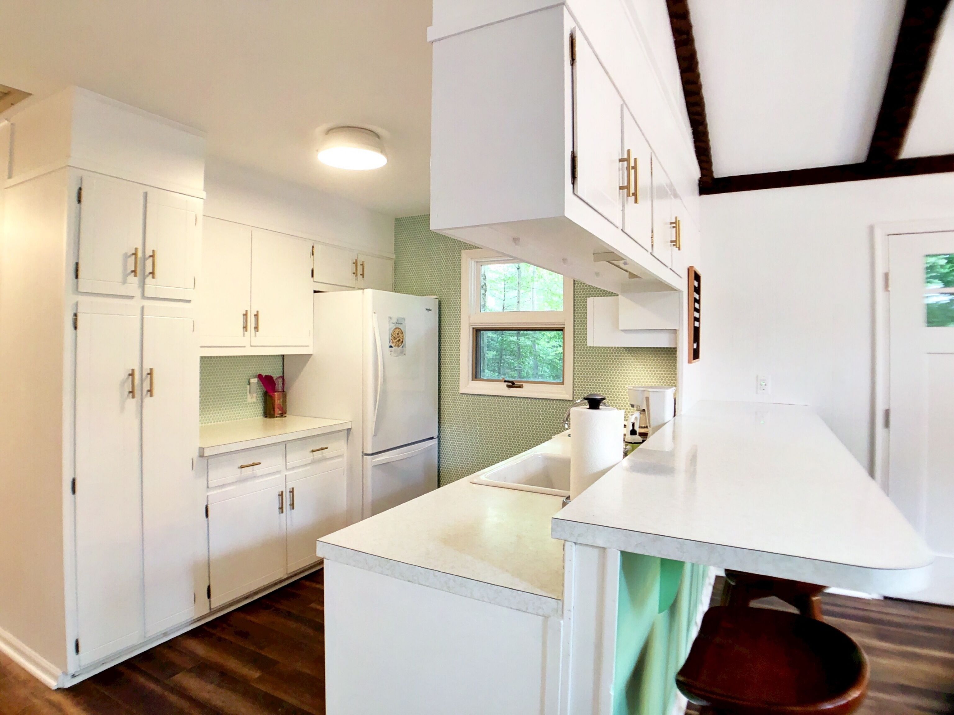 A modern kitchen with white cabinetry, a central island, and a window with a view of greenery.