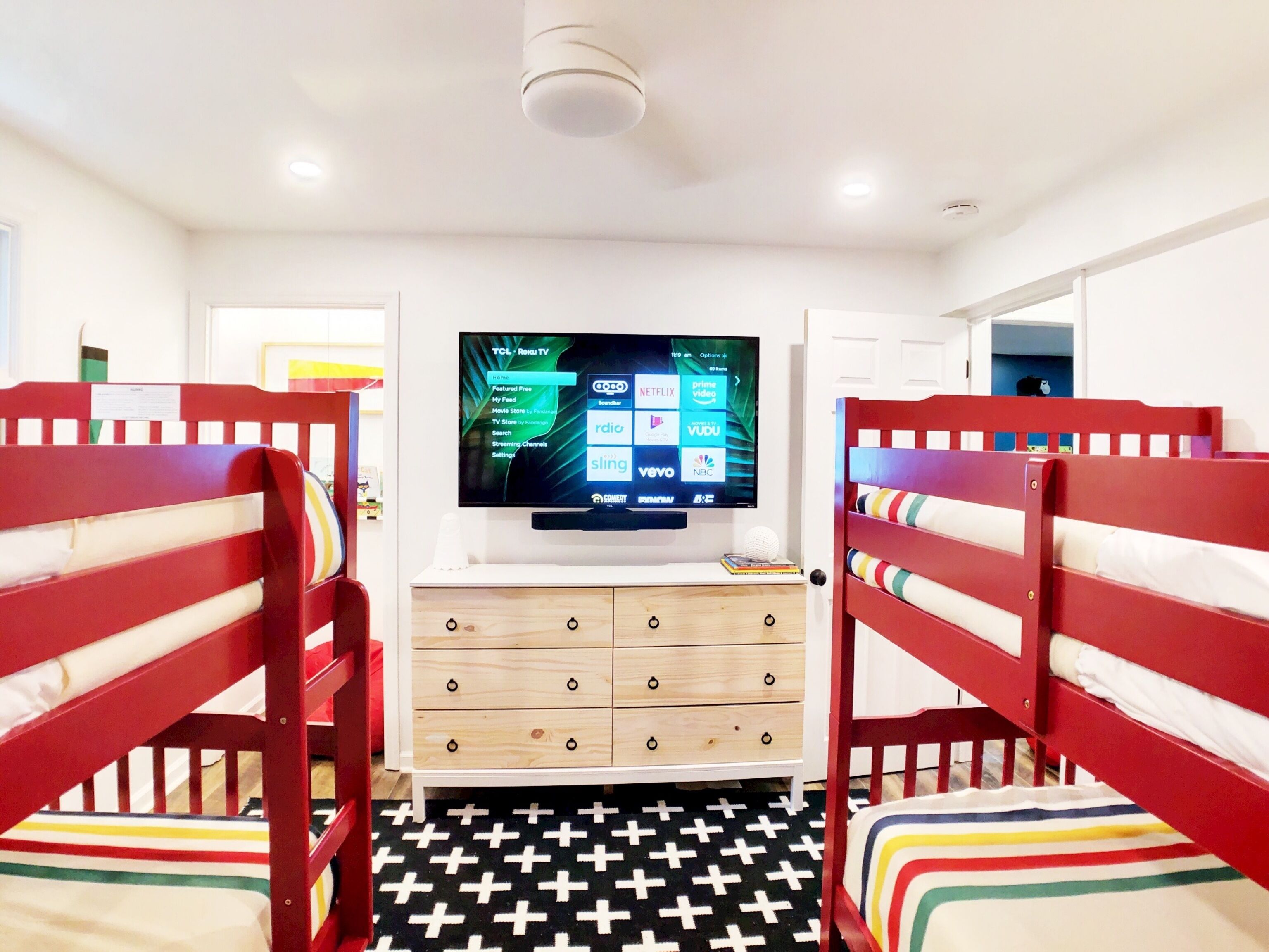 Une chambre avec des lits superposés, un téléviseur fixé au mur, une commode et un sol à motifs.