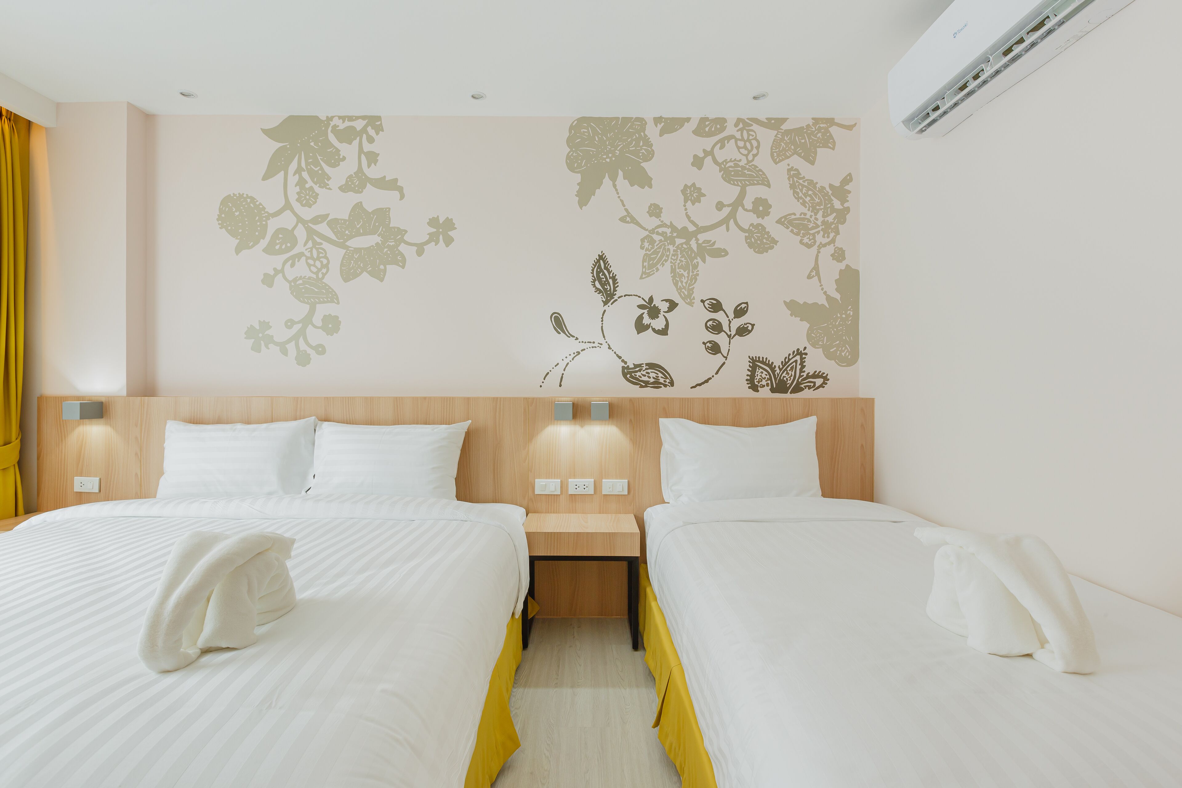 A hotel room with two beds, a wooden headboard, wall-mounted lights, and a floral wall decal.
