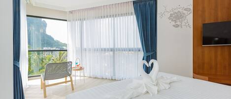 Habitación de hotel con una cama grande, televisión, sillón y vista a la montaña.