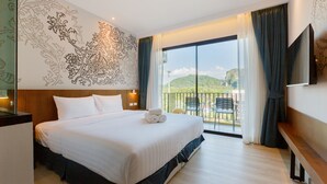 Une chambre d’hôtel avec un grand lit, un balcon offrant une vue sur les collines et un téléviseur à écran plat fixé au mur.
