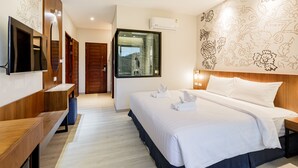 Une chambre d’hôtel moderne avec un grand lit, un téléviseur fixé au mur, un banc en bois et une vue à travers une porte vitrée.