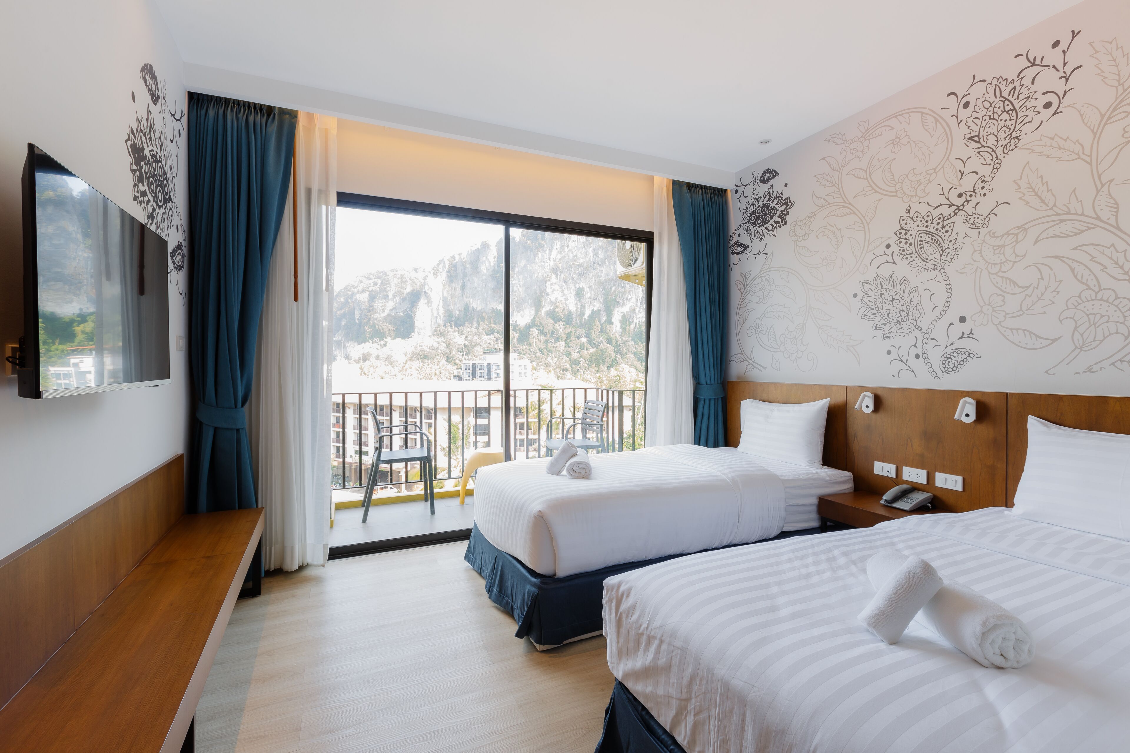 Une chambre d’hôtel avec deux lits, un banc, une télévision et un balcon offrant une vue sur les montagnes.