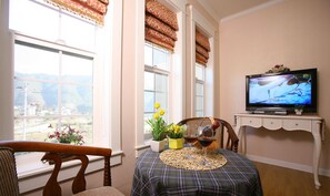 Ein gemütliches Wohnzimmer mit Fernseher, einem Esstisch mit Unterlage und einem Fenster mit Vorhängen.