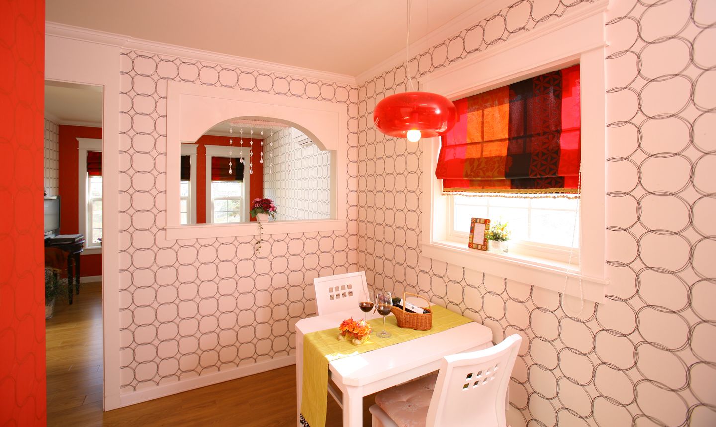 A room with a patterned wall, a window with a red blind, a table with a yellow tablecloth, and a white chair.
