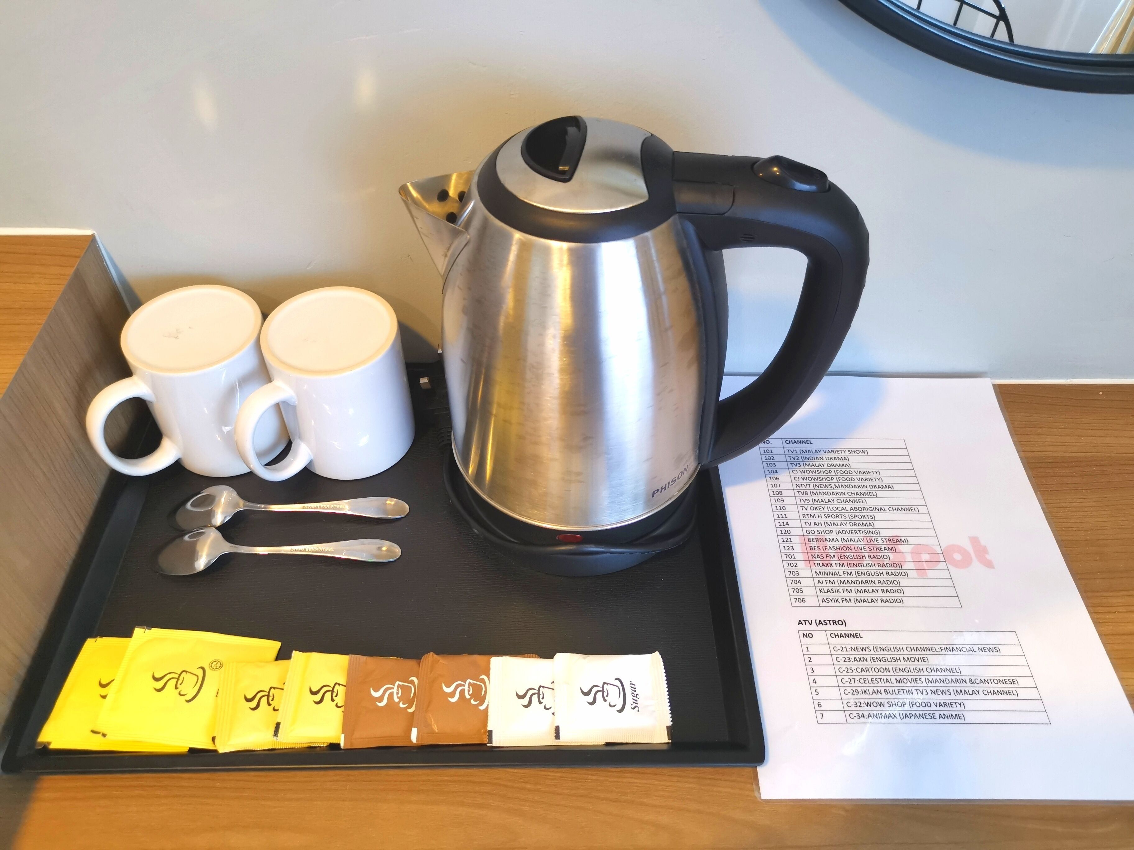 A tray with a stainless steel electric kettle, two white mugs, two spoons, and packets of sugar.