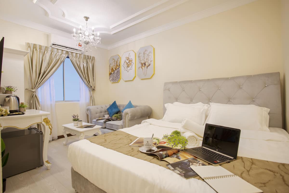 A hotel room with a bed, a desk with a laptop, a sofa, and a chandelier.