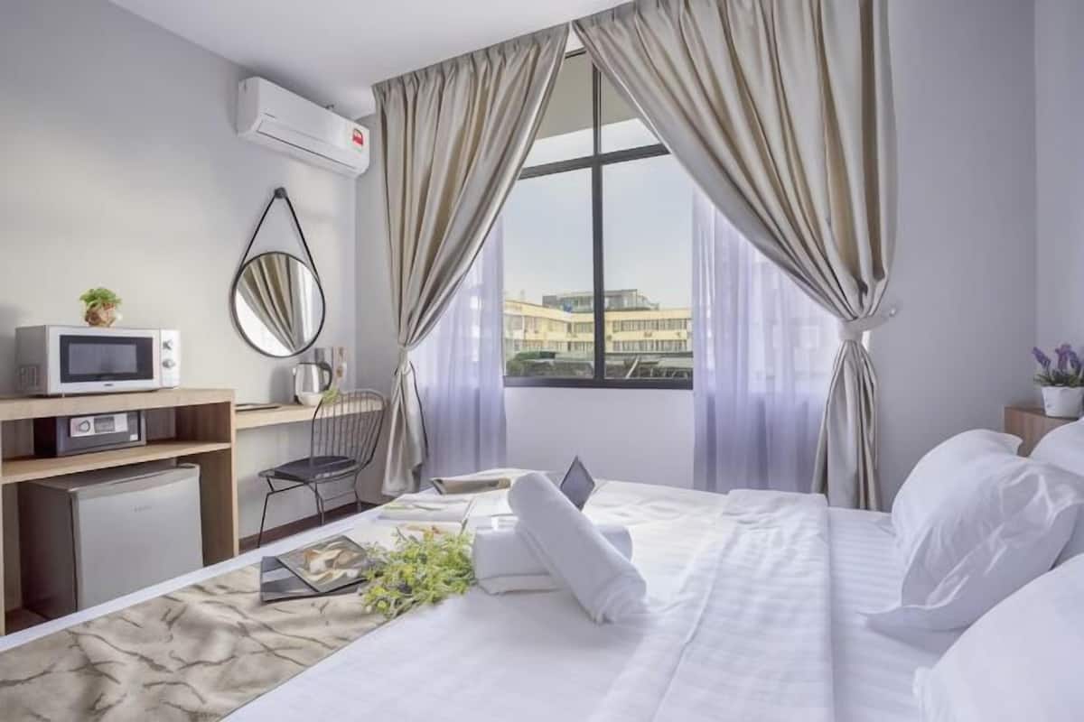 A hotel room with a bed, a desk with a computer, a chair, a TV, and a window with curtains.