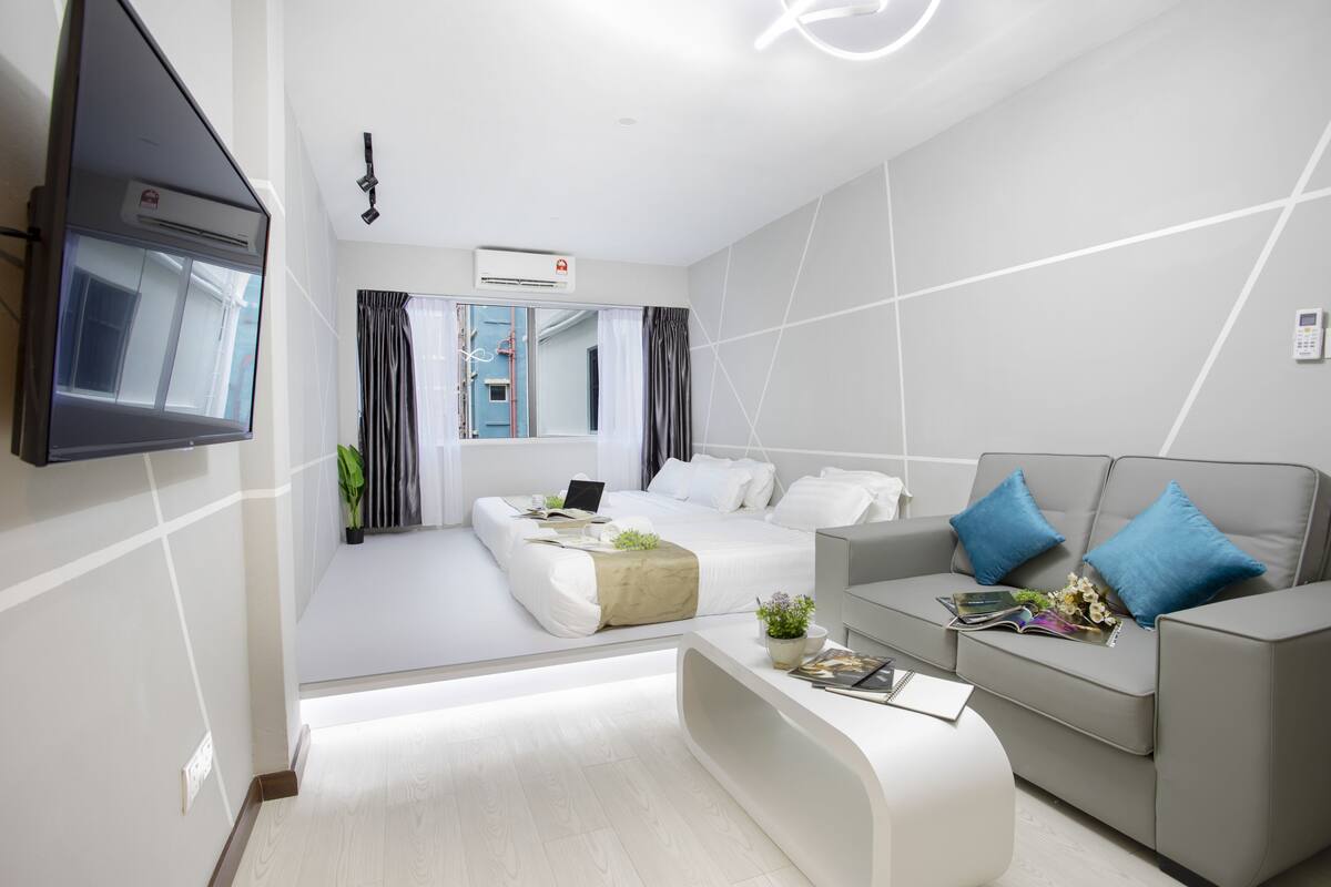 A modern hotel room with a bed, a sofa, a coffee table, and a TV mounted on the wall.