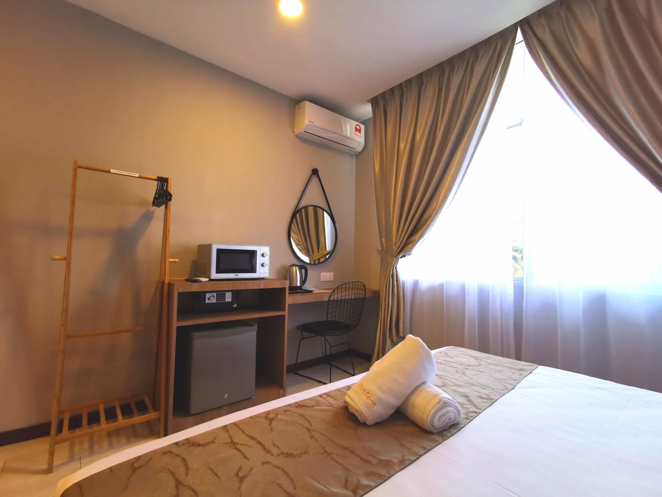 Ein Hotelzimmer mit Bett, Schreibtisch mit Mikrowelle, kleinem Kühlschrank, Stuhl, Wandspiegel und Klimaanlage.