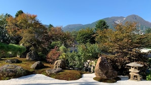 Un jardín japonés tradicional con rocas grandes, un farol de piedra y montañas al fondo.