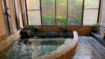 A spa area with a stone hot tub, wooden walls, and large windows overlooking a bamboo forest.