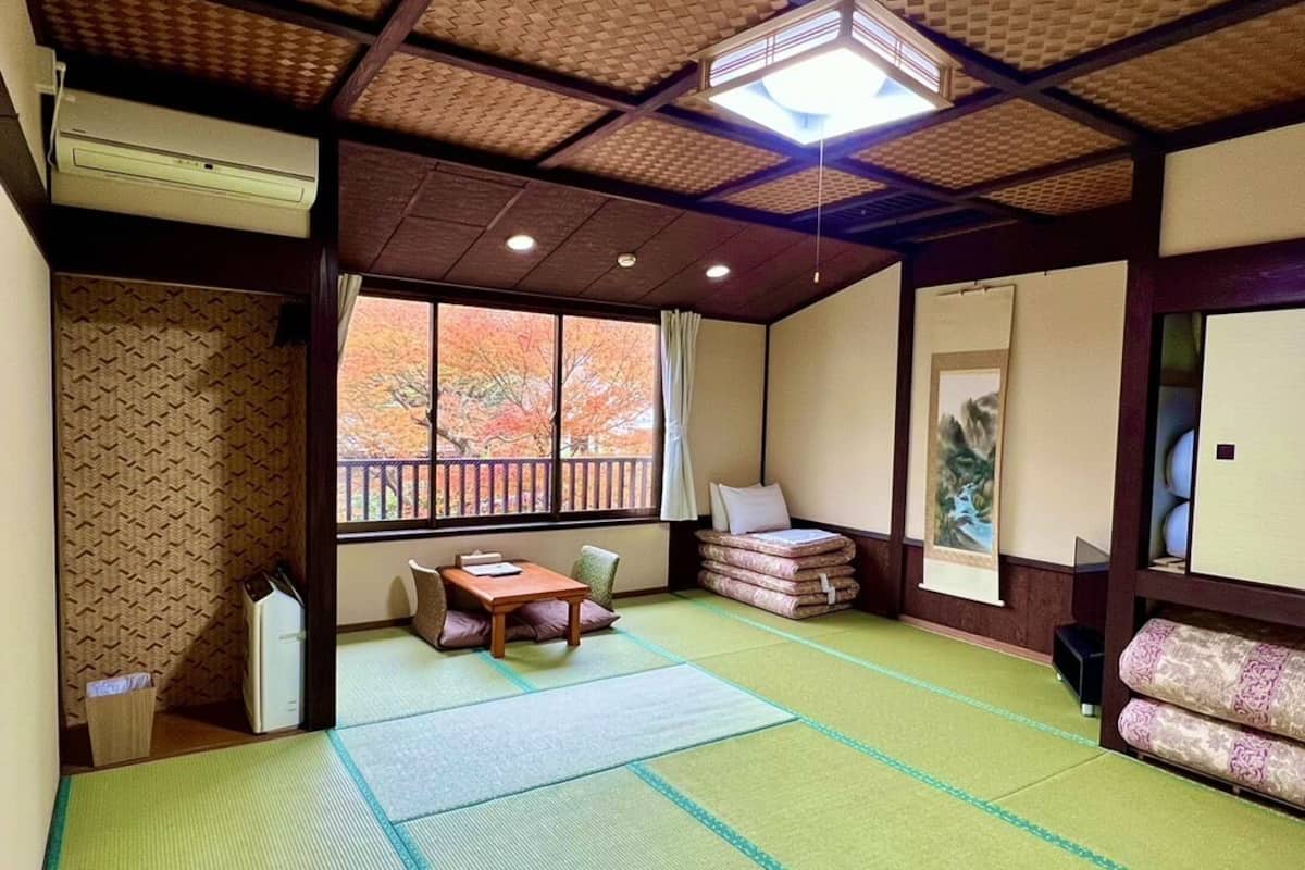Ein traditioneller japanischer Raum mit Tatami-Bodenbelag, einer Schiebetür, einem Fenster mit Herbstlaub und einem Tisch aus Tatami-Matten sowie einer niedrigen hölzernen Bank.
