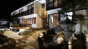 Un edificio moderno de dos pisos con una entrada bien iluminada, un sendero de piedra y un farol tradicional japonés.
