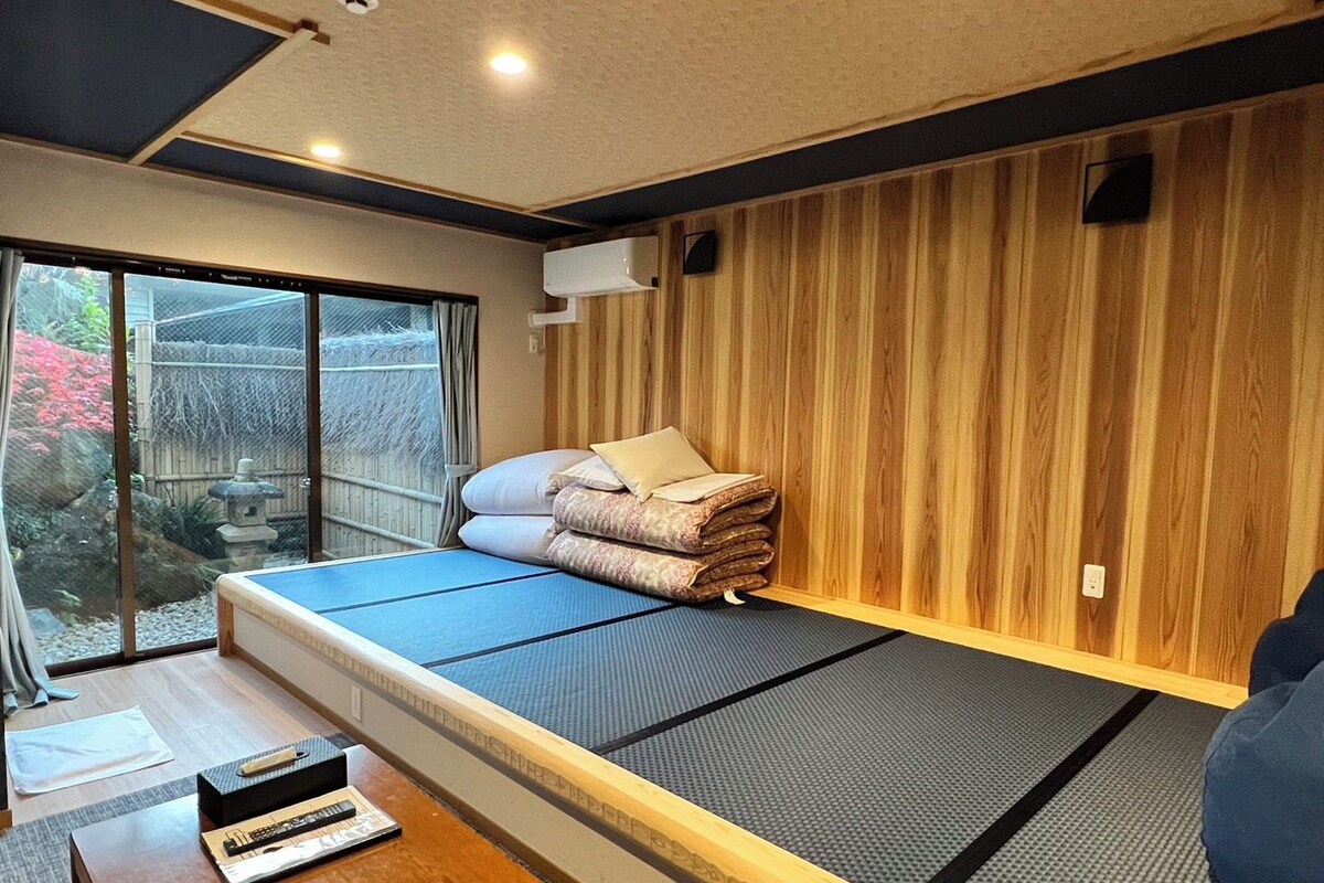 Ein Zimmer mit einem Bett, einer Holzwand, einem Fenster und einem kleinen Tisch.