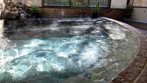 Un jacuzzi con agua cristalina, rodeado de baldosas de piedra y plantas en macetas.