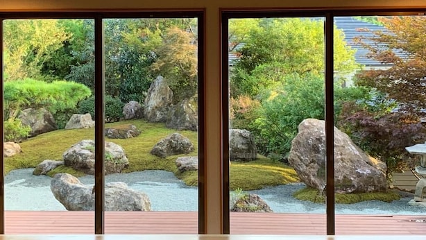Vista a través de amplios ventanales de un jardín con rocas y follaje.