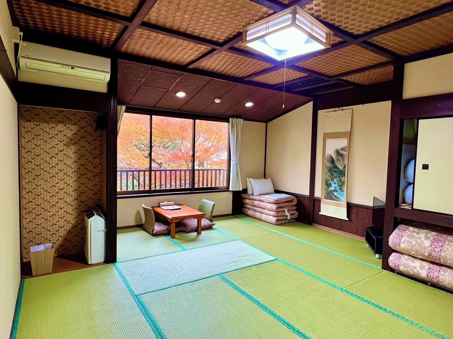 Um quarto japonês tradicional com tatames, uma mesa baixa, almofadas, uma janela com folhagem de outono e um ventilador de teto.