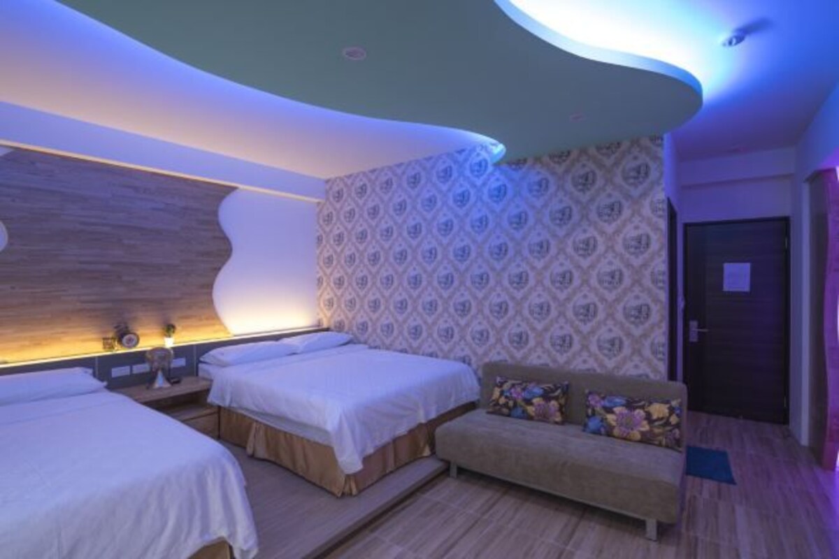 A hotel room with two beds, a sofa, and a patterned wallpaper.