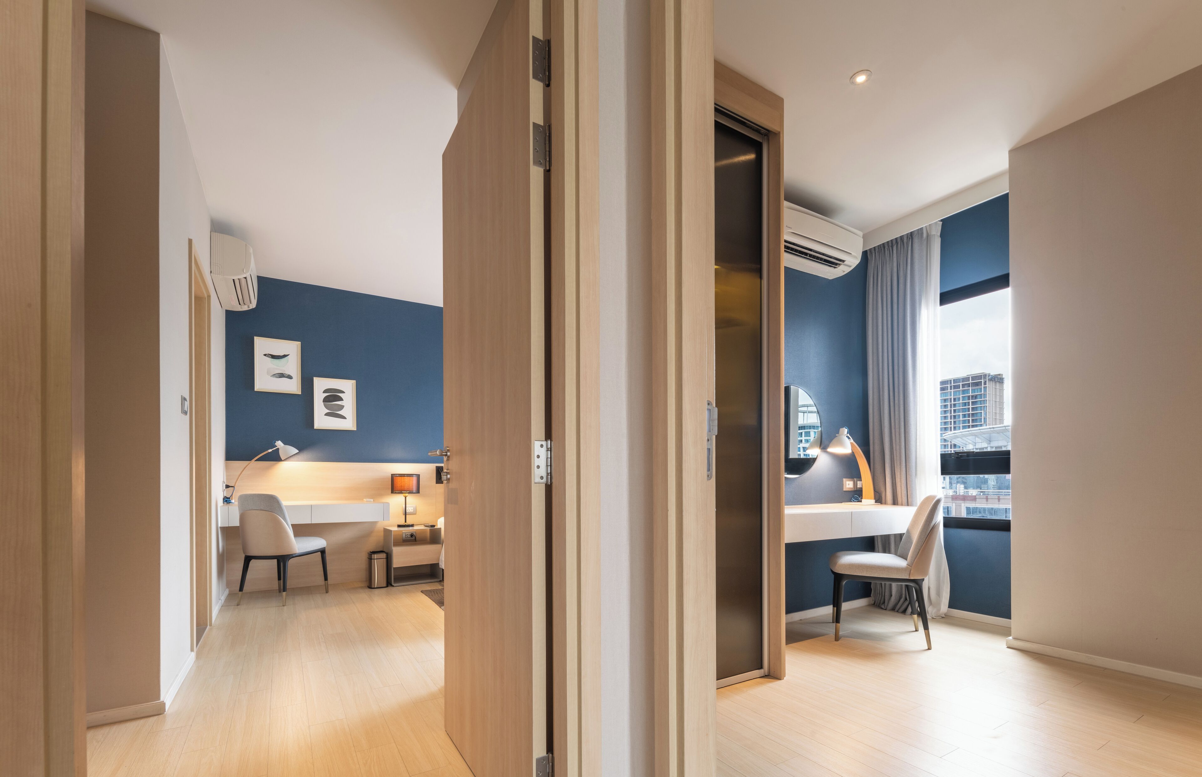 A modern hotel room with a desk, chair, and a view of the city through a large window.