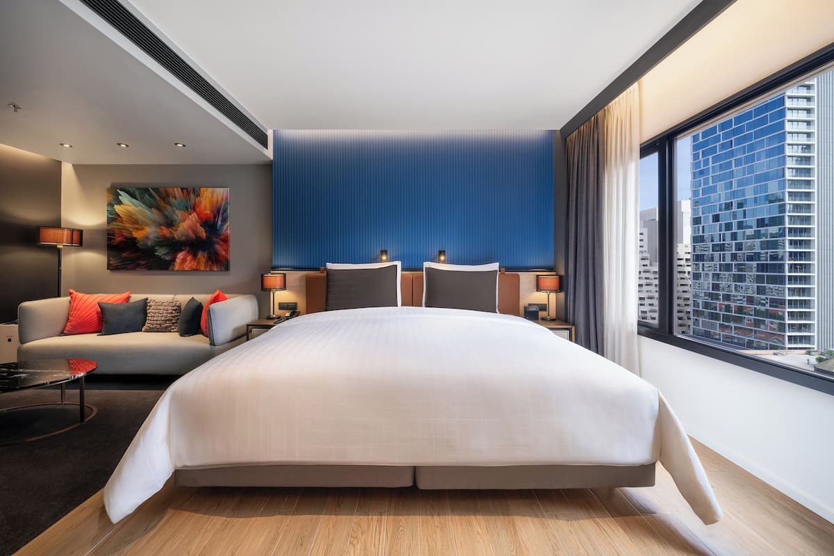 Habitación de hotel moderna con una cama grande, un sofá y vistas a la ciudad.
