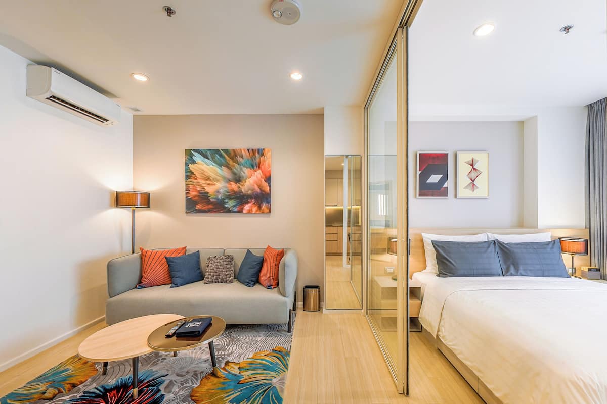 Una habitación de hotel moderna con sofá, una mesita redonda, una cama y un separador de vidrio.