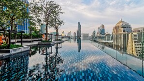 A rooftop infinity pool with a cityscape view, surrounded by trees and modern buildings. - Sindhorn Midtown Hotel Bangkok, Vignette Collection by IHG (Bangkok)