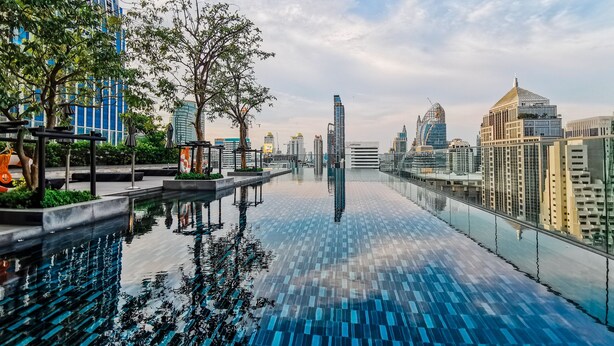 Una piscina infinita en la azotea con vistas a un paisaje urbano, rodeada de árboles y edificios modernos.
