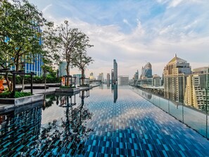 A rooftop infinity pool with a cityscape view, surrounded by trees and modern buildings. - Sindhorn Midtown Hotel Bangkok, Vignette Collection by IHG (Bangkok)