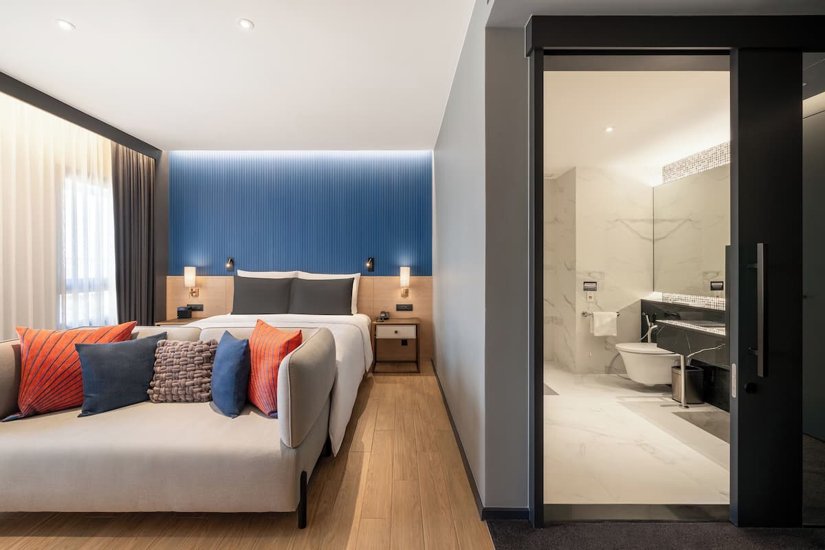 Una habitación de hotel moderna con cama, mesitas de noche, baño con ducha y vistas a la ciudad.