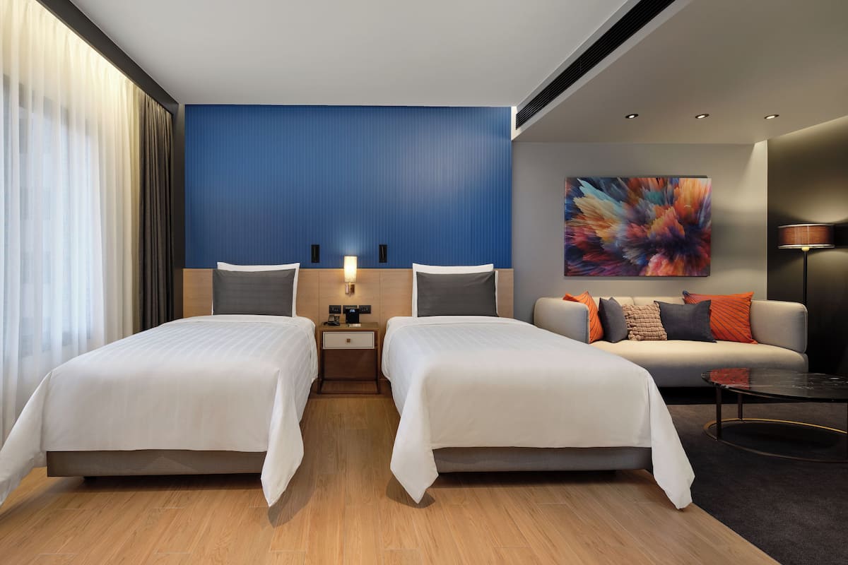 Una habitación de hotel moderna con dos camas, un sofá, una mesita de centro y un cuadro en la pared.