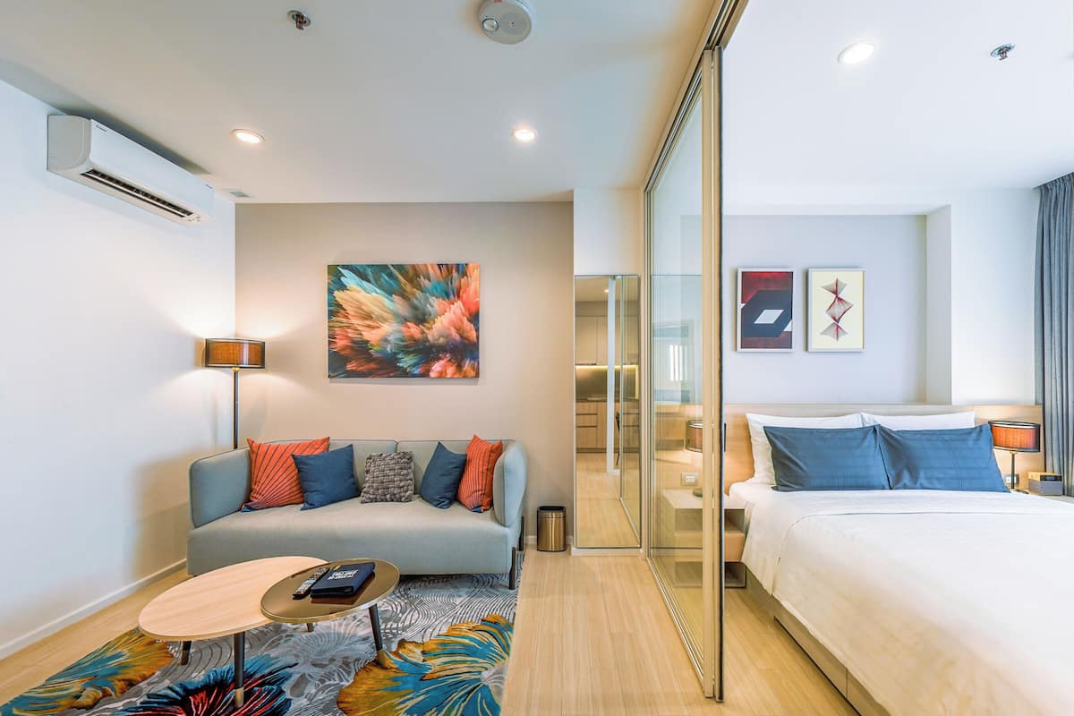Una habitación de hotel moderna con sofá, cama, una mesita y un separador de vidrio.