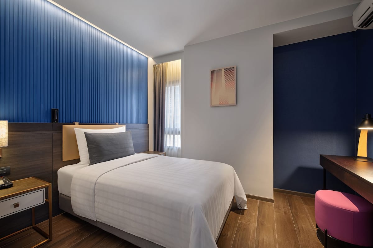 Una habitación de hotel moderna con una cama grande, un escritorio, una silla y una mesita de noche.