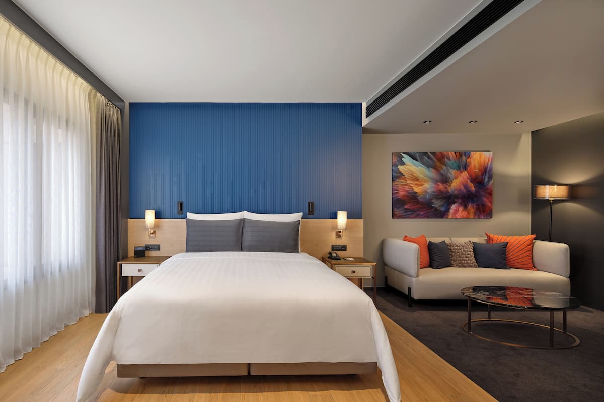 Una habitación de hotel moderna con una cama grande, un sofá, una mesa de centro y un cuadro en la pared.