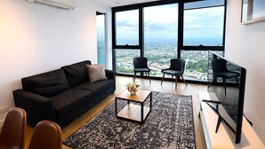 Una sala de estar moderna con un sofá negro, dos sillas negras, una mesa de centro y un amplio ventanal con vistas a la ciudad.